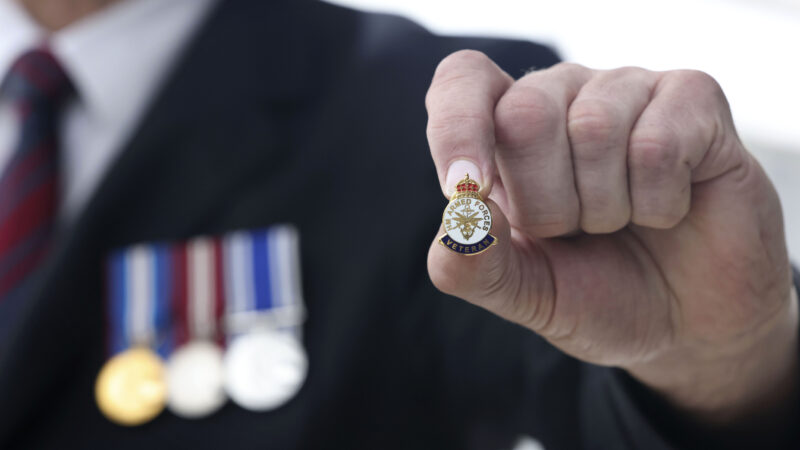 A veteran holding up a veterans badge with medal on his chest.