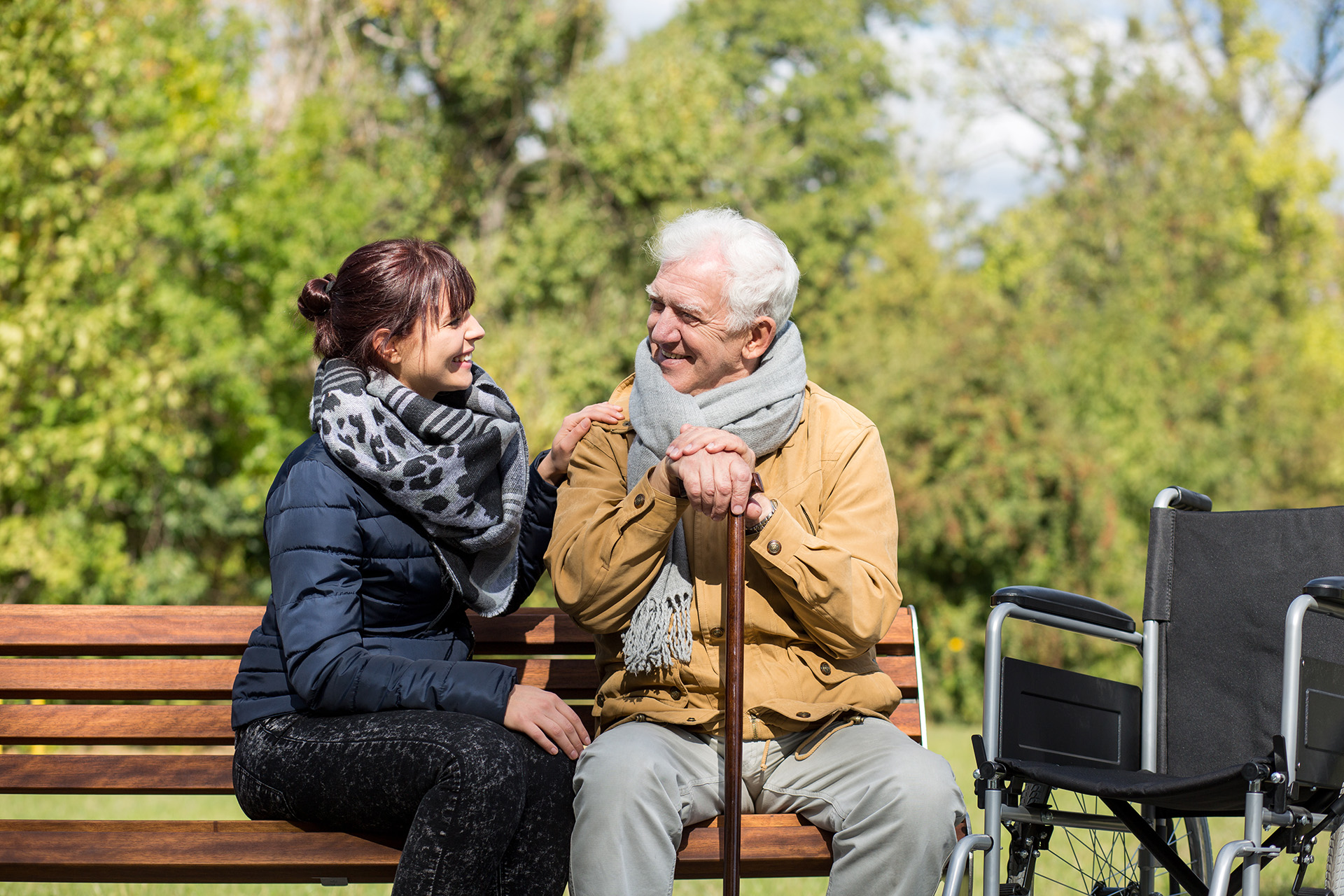 A young female carer sitting on a bench beside an elderly veteran.