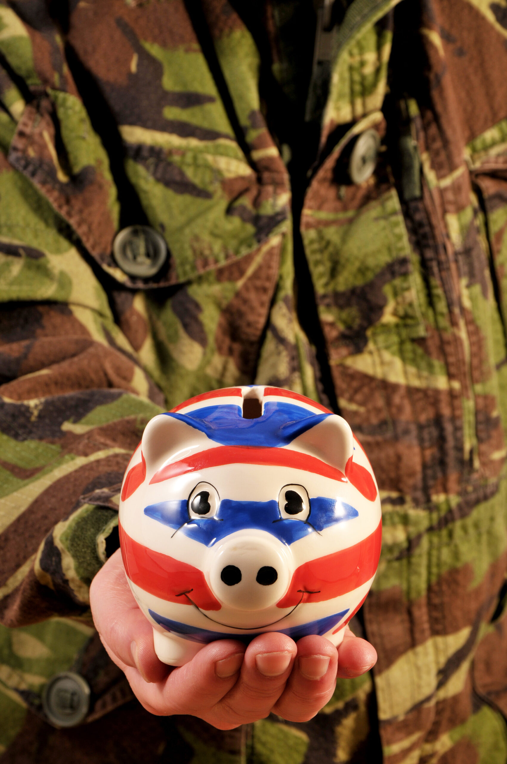 A uniformed soldier holding a Union Flag piggy bank, symbolising armed forces pensions advice.