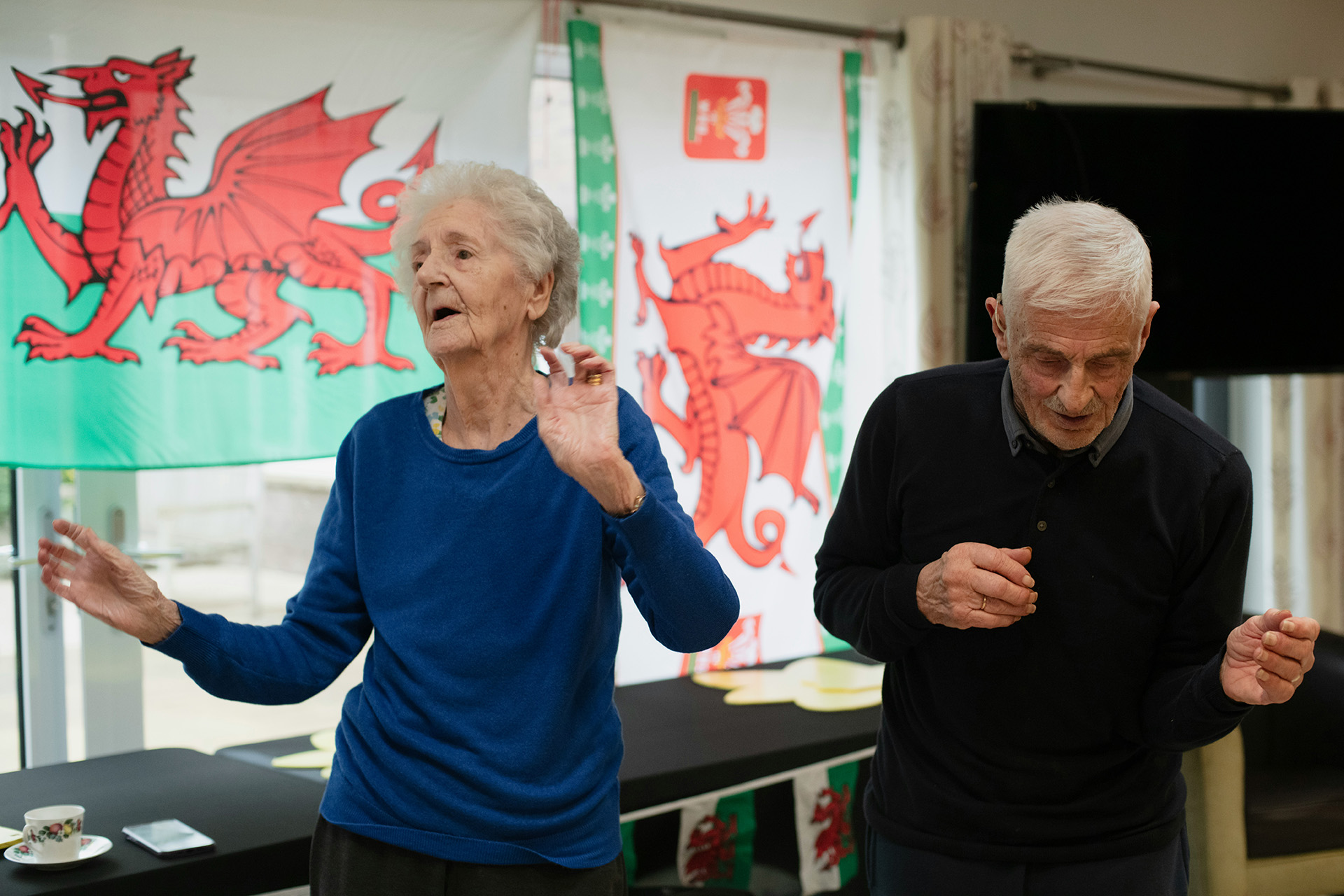 Two elderly people dancing in front of Welsh flags, highlighting physical health support for veterans in Wales.